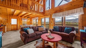 A spacious wooden cabin with a loft bedroom, a dining area, and a living room with two leather sofas and a coffee table.
