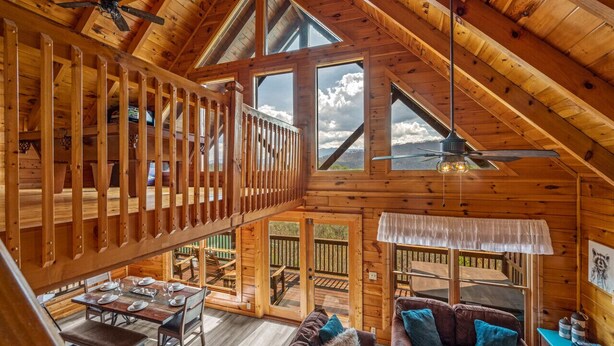 A spacious wooden cabin with a high ceiling, a balcony with a railing, and a dining area with a table set for four.