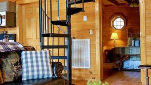 A cozy cabin interior with a spiral staircase, a leather sofa, a round coffee table with a plant, and a small dining area. - Mountain Mist - Secluded Cabin, MTN View, Hot Tub! (Sevierville)