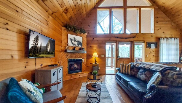 A cozy cabin interior with a fireplace, wooden walls, a sofa, and a television. - Mountain Mist - Secluded Cabin, MTN View, Hot Tub! (Sevierville)