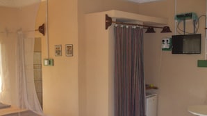 A hotel room with a bed, a shower area with a curtain, a small sink, and a television mounted on the wall. - Camping-Sukuta & Lodge (Serrekunda)