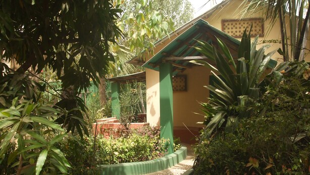 A garden pathway leading to a building with a green roof and a small structure. - Camping-Sukuta & Lodge (Serrekunda)