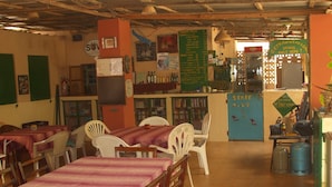 A restaurant with tables and chairs, a menu board, and a sign indicating drinks are only available at the bar. - Camping-Sukuta & Lodge (Serrekunda)