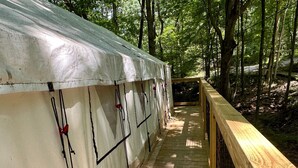 A wooden deck leading to a white tent-like structure with black lines and red clips, surrounded by trees.