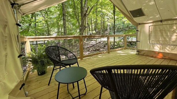 A covered outdoor area with a wooden deck, a metal railing, and two wicker chairs.