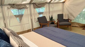 A tented accommodation with a bed, two chairs, and a small table.
