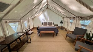 A tented room with a bed, a table, a bench, and a chair.
