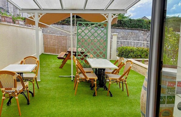 Un patio al aire libre con una mesa, sillas, césped artificial, una valla de madera y una verja verde.