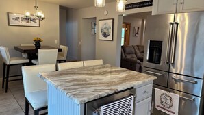 Une cuisine moderne dotée d’un plan de travail en marbre, d’appareils électroménagers en acier inoxydable et d’un coin repas avec des chaises en cuir blanc.