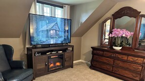 Un salon avec un téléviseur, une cheminée, un fauteuil en cuir noir, une commode en bois et un miroir.