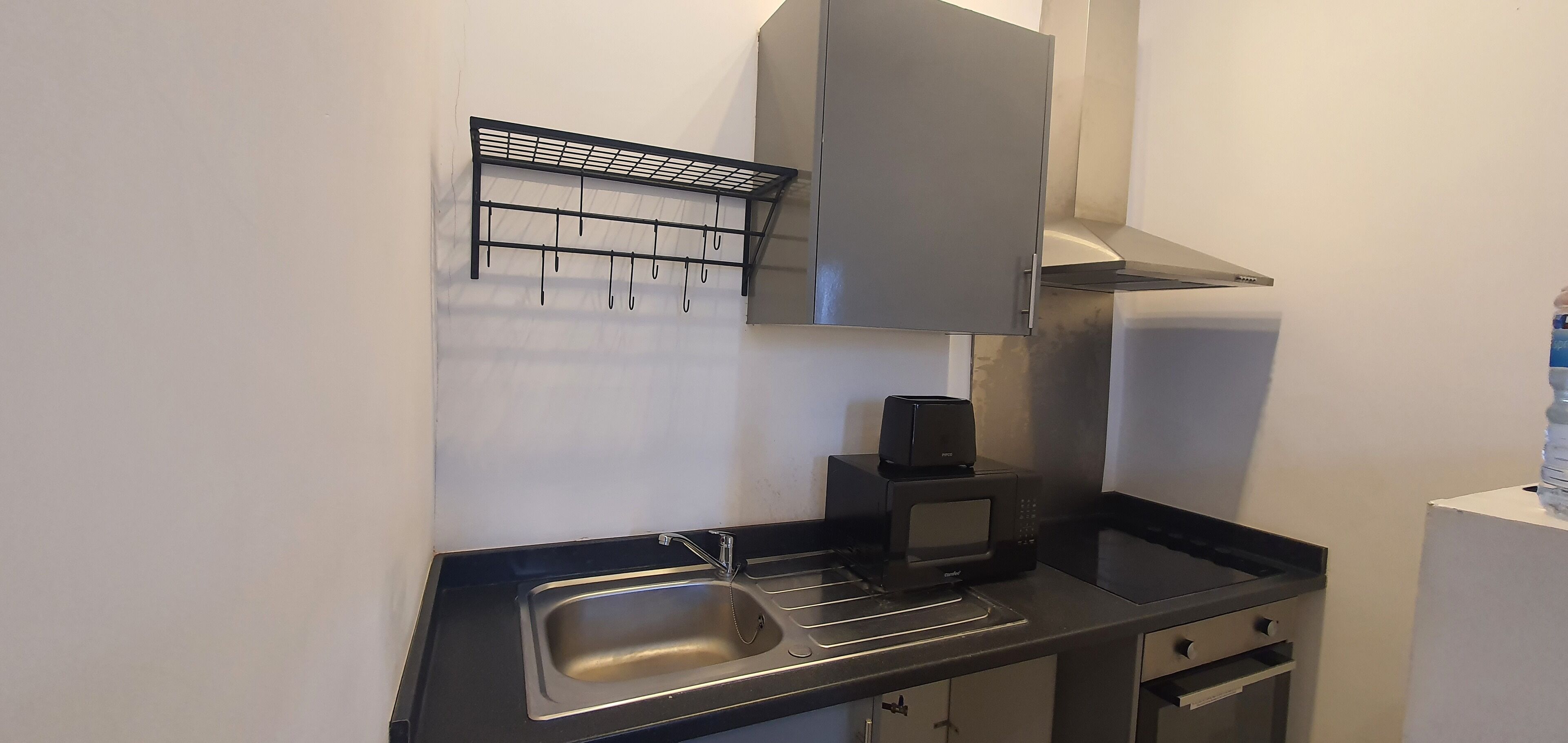 Een kleine keuken met een roestvrijstalen spoelbak, een zwarte magnetron en een zwart hangrek.