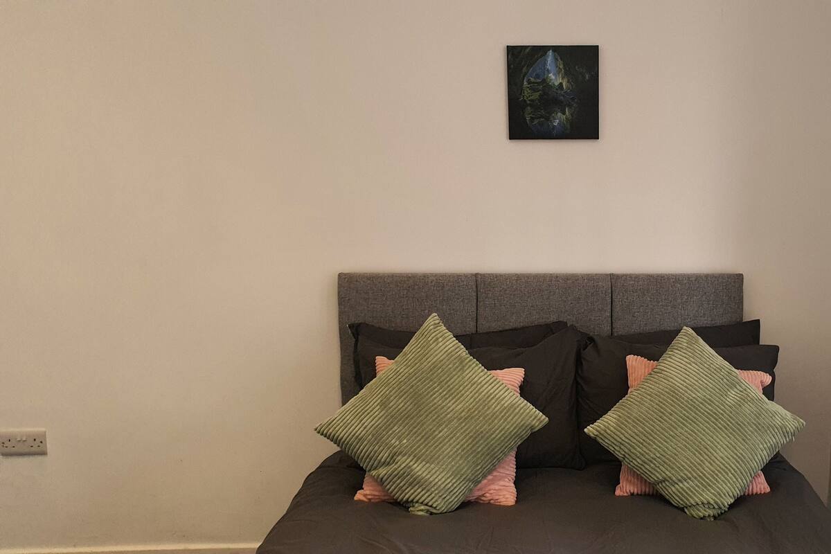 Een bed met een grijze hoofdbord en twee groene kussens.