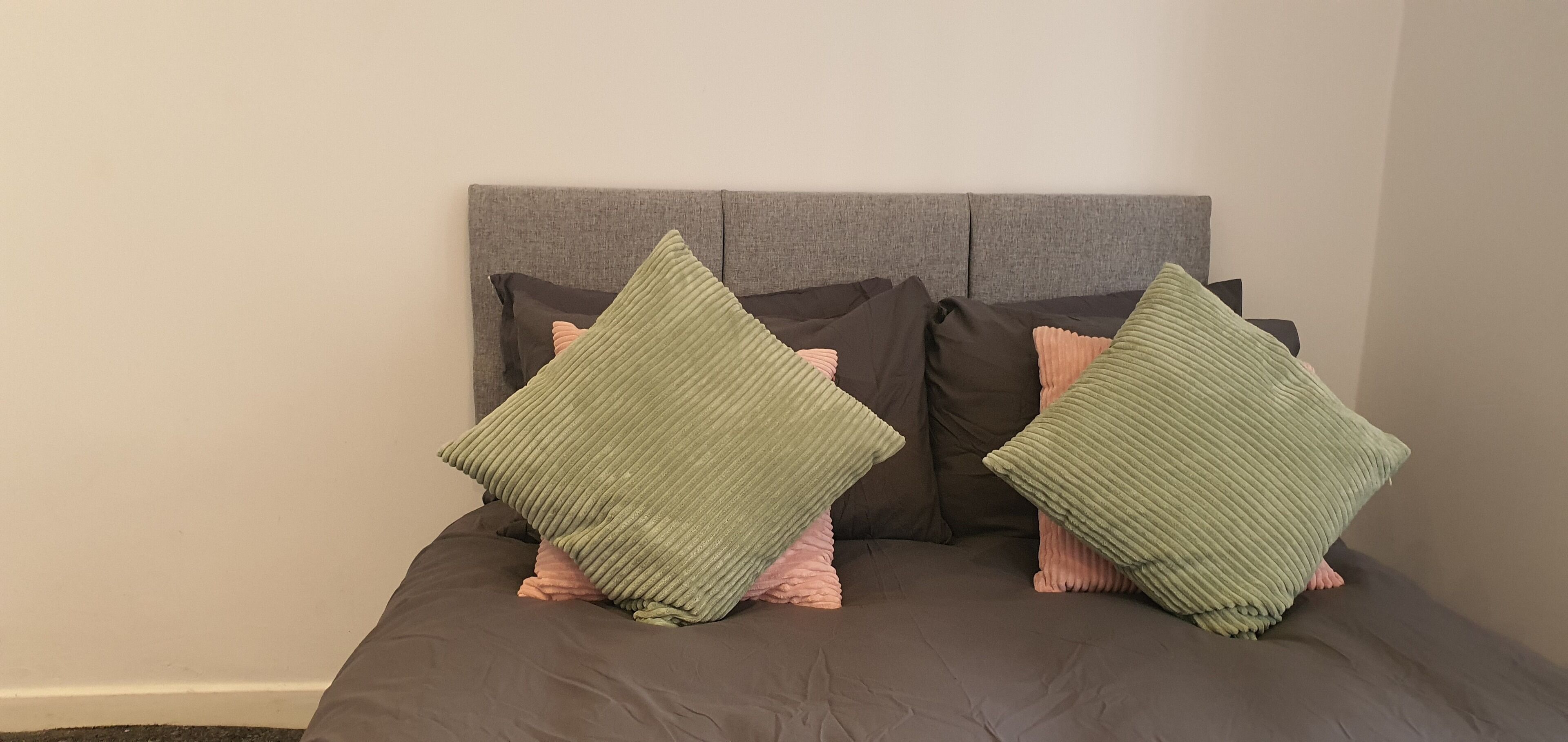 A bed with a grey headboard and two green pillows.
