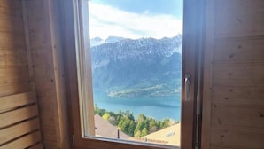 Una cabaña de madera con un ventanal grande que ofrece vistas a un lago y montañas.