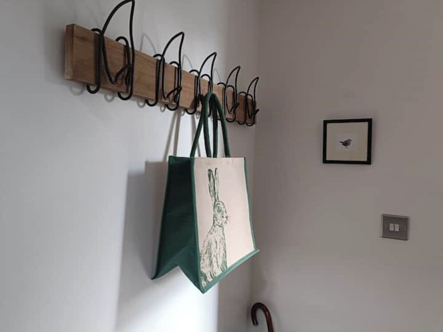 A wall-mounted coat rack with a green and white tote bag hanging from it.