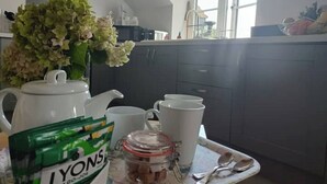 Une cuisine avec une bouilloire blanche, une tasse blanche, un bocal de collations et un plateau sur lequel se trouve un paquet de collations vert.