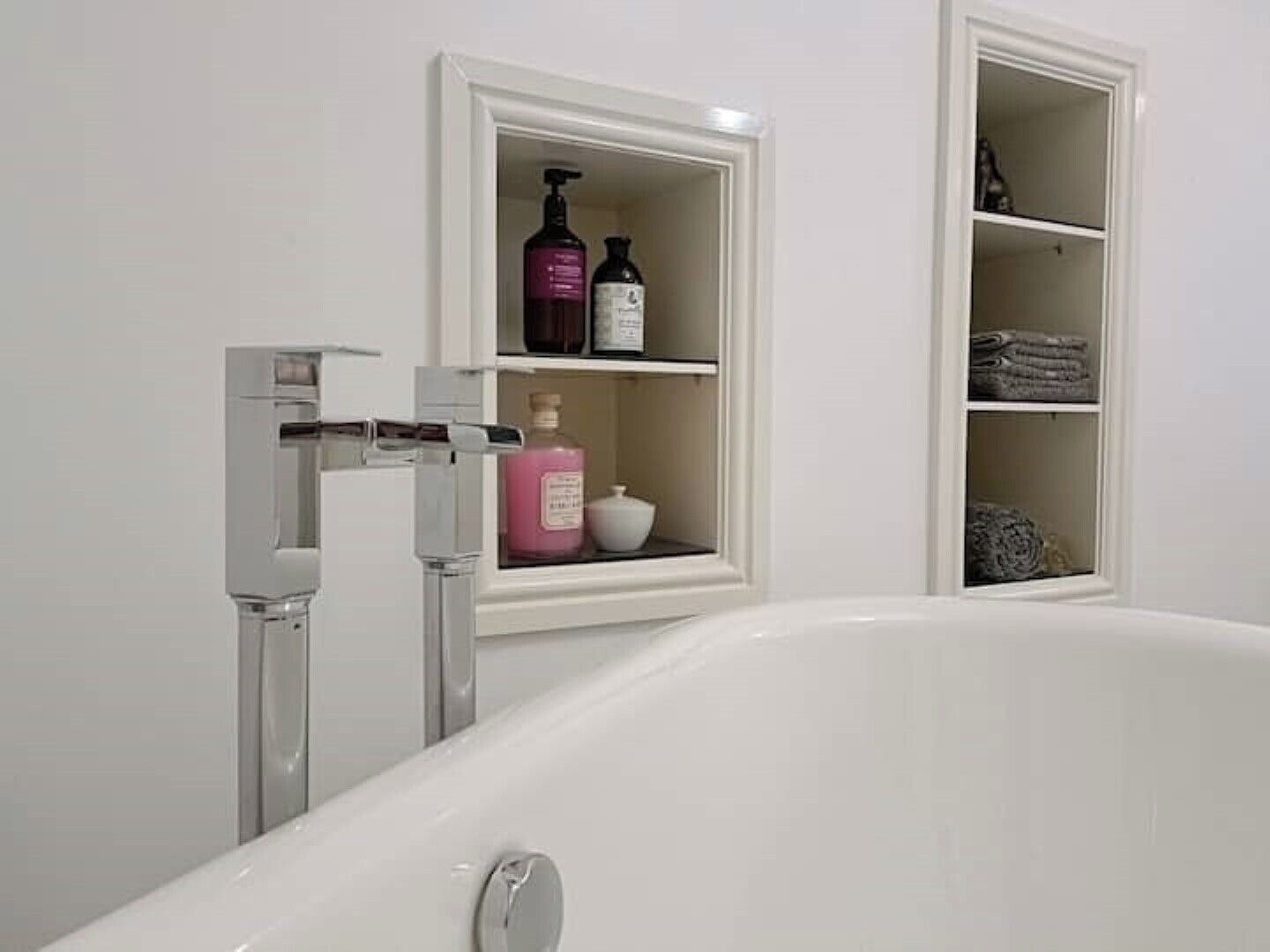 A bathroom with a freestanding bathtub, a built-in shelf with toiletries, and a towel rack.