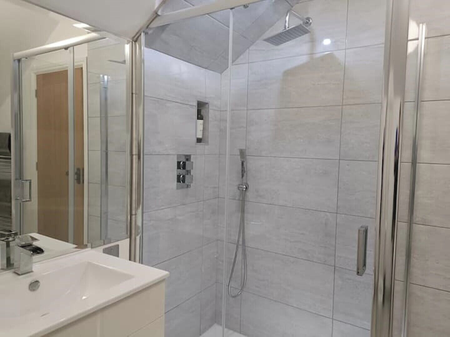 Un baño moderno con cabina de ducha de vidrio, un lavabo blanco y un espejo.