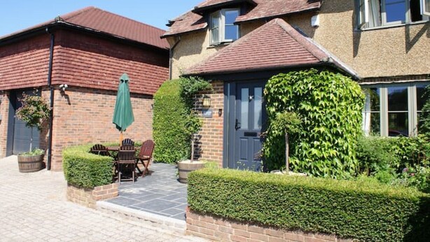 Une maison à deux étages, avec une façade en briques, un toit recouvert de tuiles et une porte d’entrée surmontée d’un auvent vert.