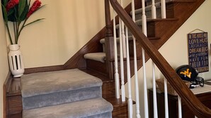 A staircase with wooden steps and white balusters, a vase with red flowers, and a motivational sign on the wall.