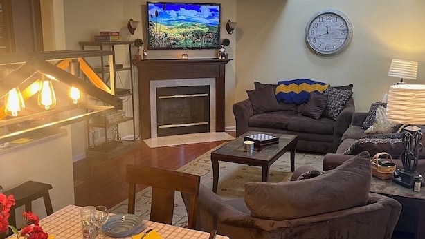 A living room with a fireplace, a television mounted above it, a sofa, a coffee table, and a dining area with a table set for two.