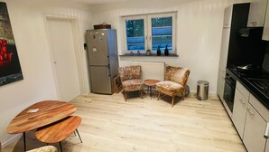 A compact kitchen with a refrigerator, stove, and dining area with chairs and a table. - Ferienwohnung "Am Landwehrgraben" (Michelau in Oberfranken)
