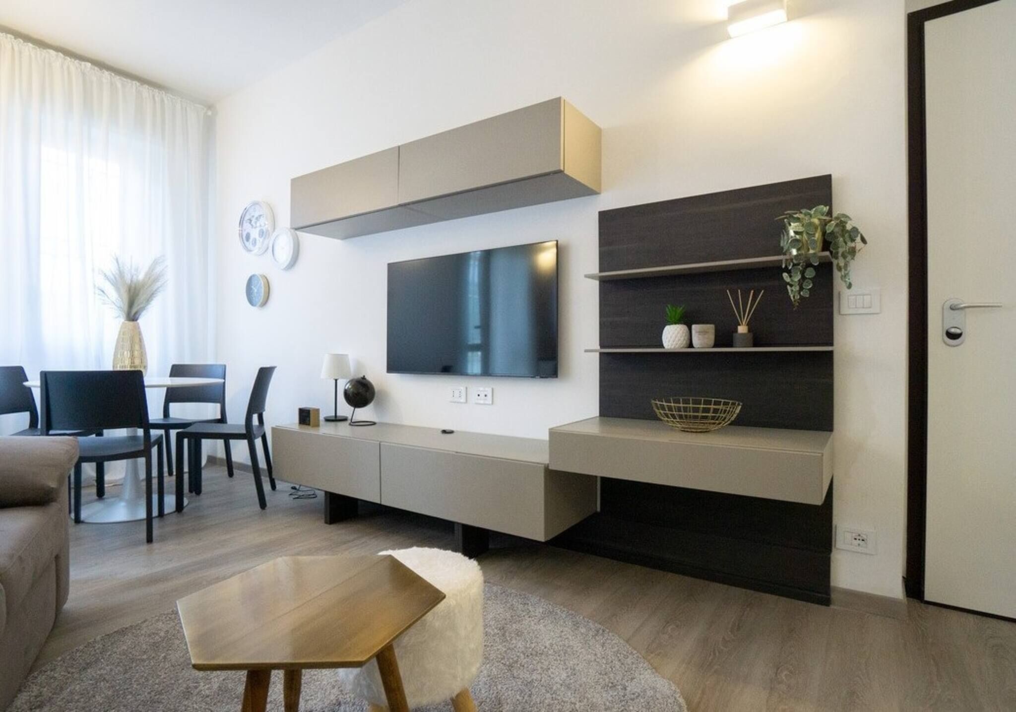 Ein modernes Wohnzimmer mit Flachbildfernseher, Einbauschränken, Essbereich mit Stühlen und einer Couch.