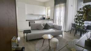 A modern living room with a sofa, a small table, a round rug, and a kitchen in the background. - Charming & Modern 3br apt in the Heart of Asti (Asti)