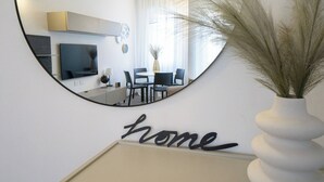 A round mirror reflecting a modern living room with a dining area, a television, and a wall-mounted clock. - Charming & Modern 3br apt in the Heart of Asti (Asti)