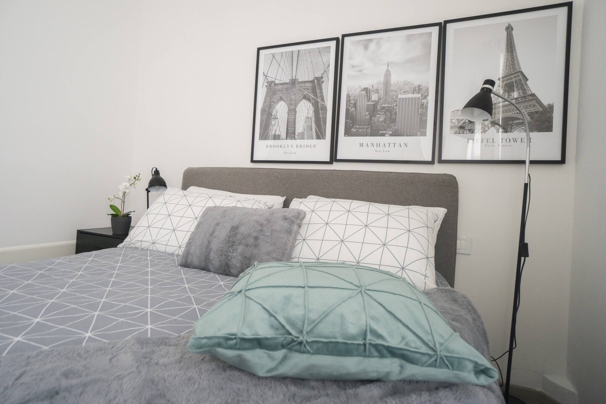 A neatly arranged bedroom with a bed, pillows, a nightstand, a lamp, and three framed pictures on the wall.