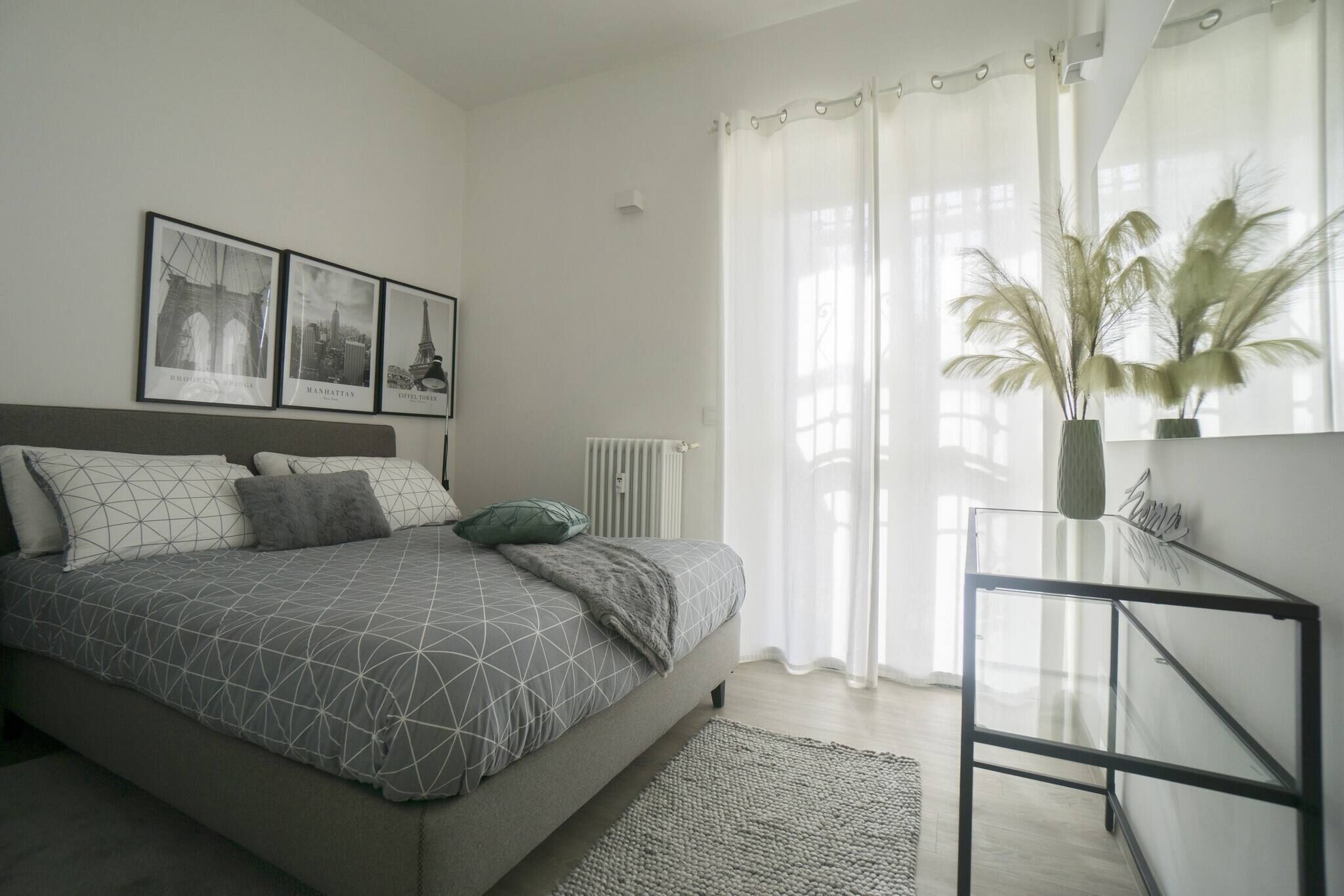 Een slaapkamer met een bed, nachtkastje, radiator en raam met dunne gordijnen.