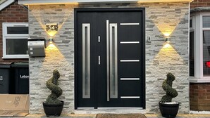 A modern house with a black front door, two potted plants, and a number plate indicating the address. - New Luxury Modern House Near Airport Free Parking (Luton)