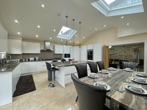 A modern kitchen with a central island, dining area with chairs, and a view of the city through skylights.