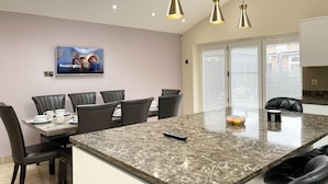 A modern kitchen with a central island, black chairs, and pendant lighting. - New Luxury Modern House Near Airport Free Parking (Luton)