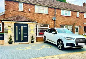 Un Audi SUV blanco estacionado frente a una casa de ladrillo con una puerta negra y una antena parabólica.