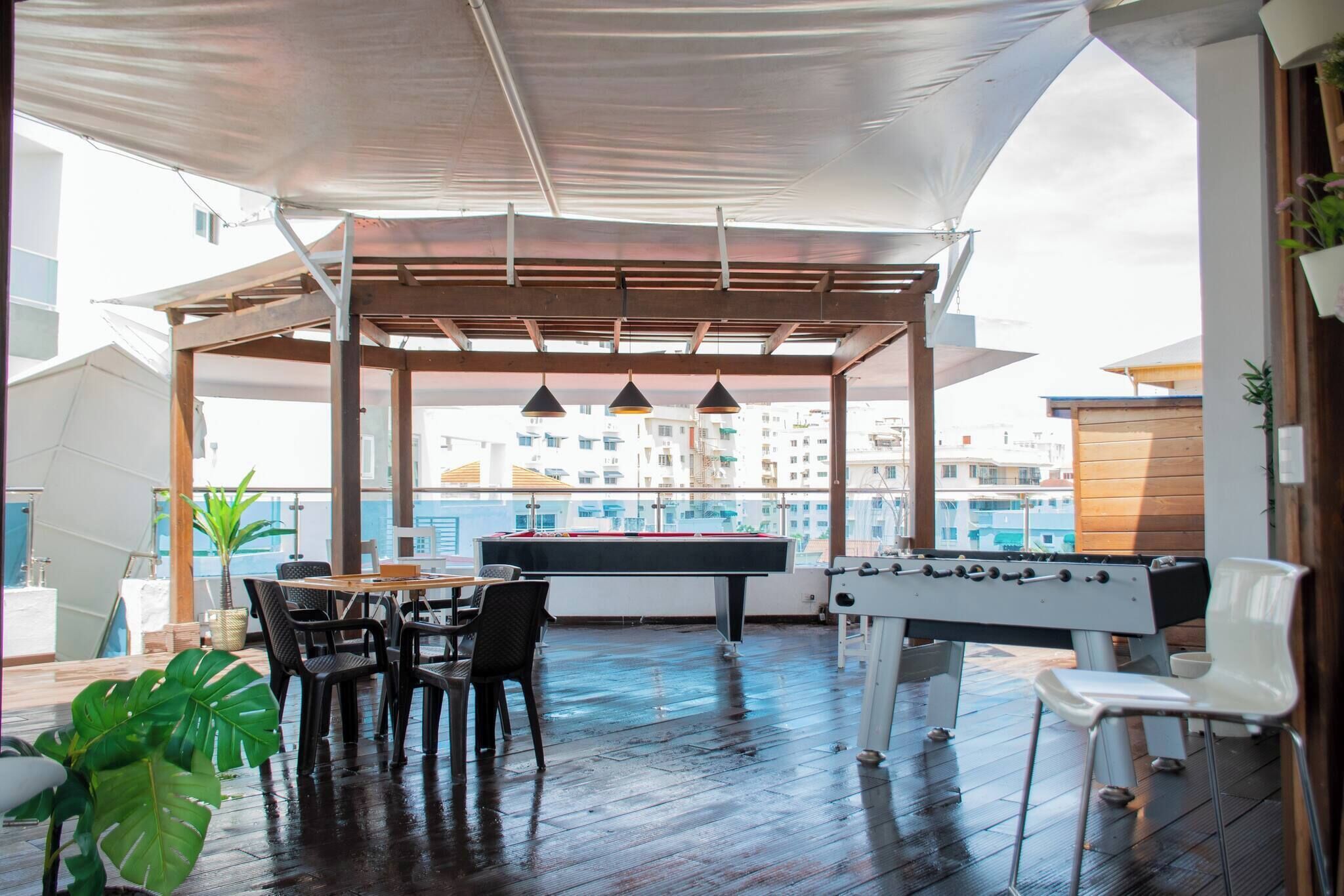An outdoor pool area with a table and chairs, a foosball table, and a view of the cityscape.