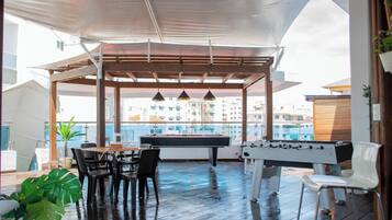An outdoor pool area with a table and chairs, a foosball table, and a view of the cityscape.