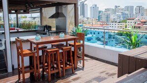 Un bar sul tetto con tavolo e sedie in legno, un barbecue e vista sulla città.