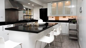 Una cucina moderna con isola centrale, sgabelli da bar bianchi, elettrodomestici in acciaio inossidabile e piano di lavoro nero.
