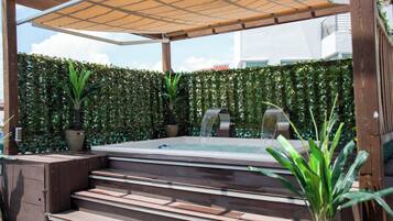 A hot tub with steps, surrounded by a wooden pergola and a hedge.