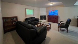 A living room with a black leather sofa, a wooden coffee table, a TV, a fireplace, and a bookshelf.