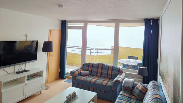 A living room with a flat-screen TV, a sofa, a coffee table, and a balcony with a table and chairs. - Apartment Brockenblick in the Harz Mountains - Pool & Sauna (Braunlage)