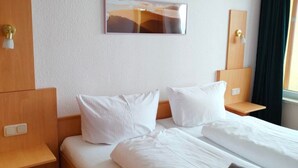A hotel room with a bed, two bedside tables, a wall-mounted light, and a window with curtains. - Apartment Brockenblick in the Harz Mountains - Pool & Sauna (Braunlage)