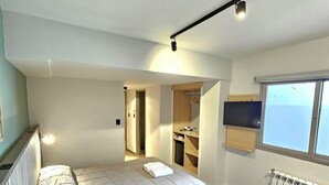 A modern bedroom with a large bed, a built-in wardrobe, a small kitchenette, and a view through a window. - M383 Hotel Bariloche (San Carlos de Bariloche)