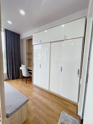 A modern room with a wooden floor, a desk, a chair, and a large white wardrobe with multiple doors. - Amy Apartment Hue (Hue)