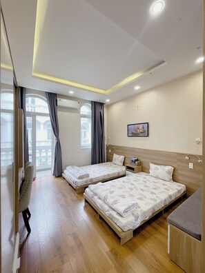 Ein Hotelzimmer mit zwei Betten, einem Schreibtisch, einem Stuhl, einem Fenster mit Vorhängen und einer Deckenleuchte.