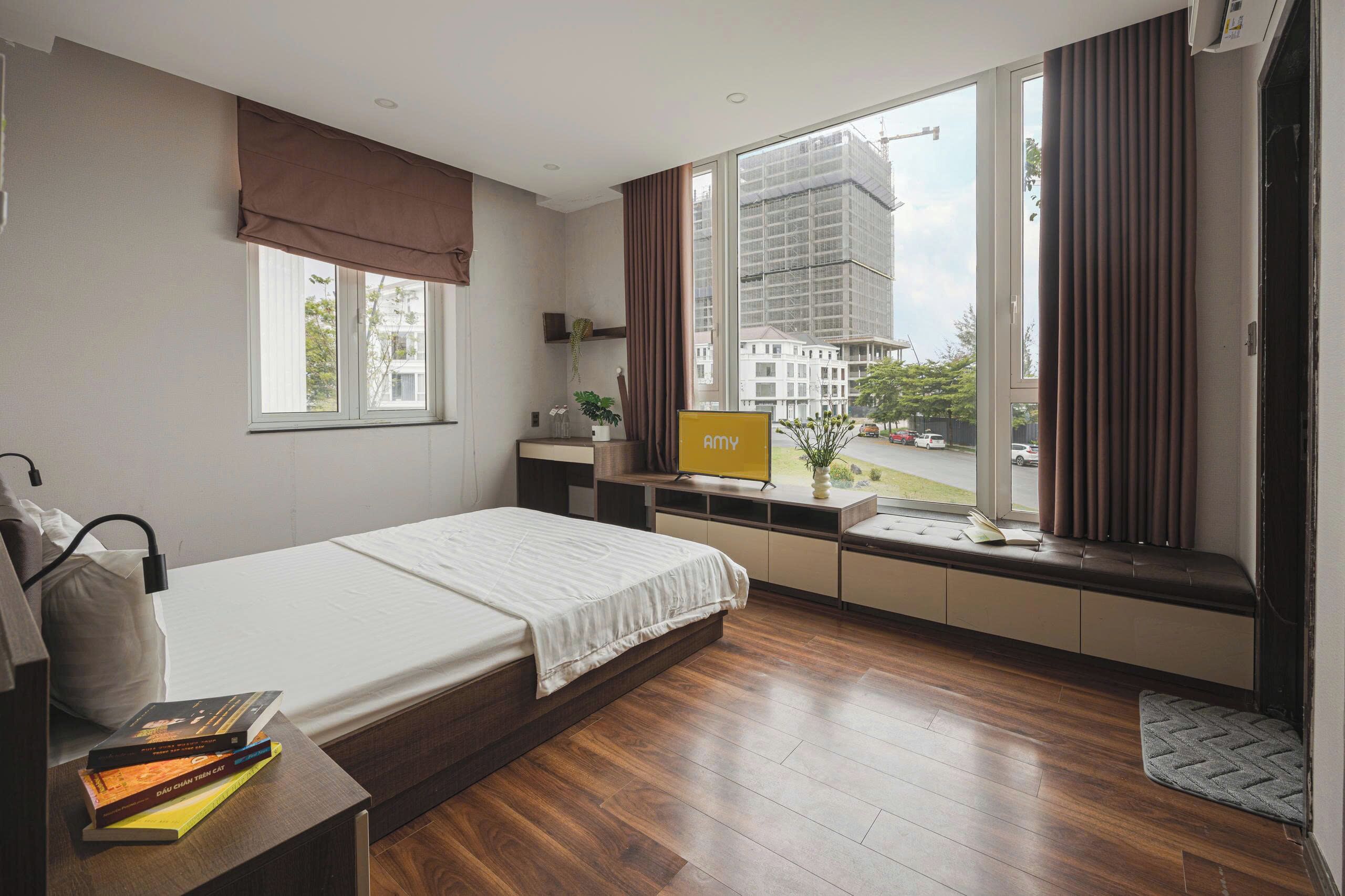 Un dormitorio moderno con cama, mesita de noche y vistas a la ciudad a través de amplias ventanas.