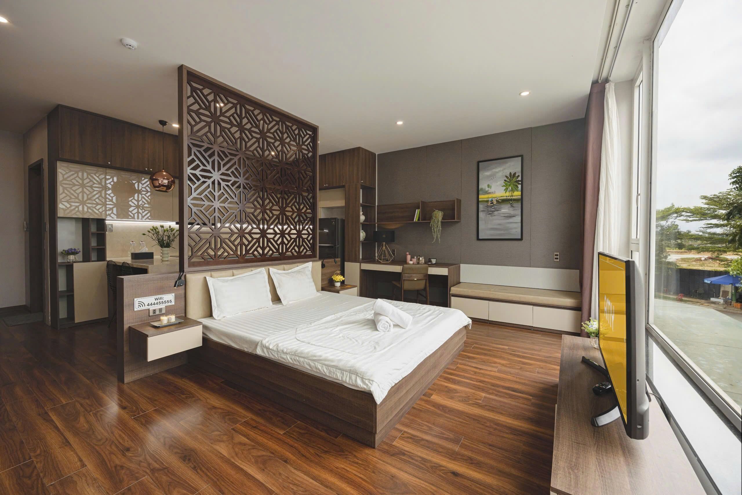 A modern hotel room with a large bed, a desk, a seating area, and a view of the outdoors.
