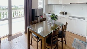 A modern kitchen with white cabinets, a dining table with chairs, and a view of the city through large windows. - Phu My An Apartment Hue (Hue)