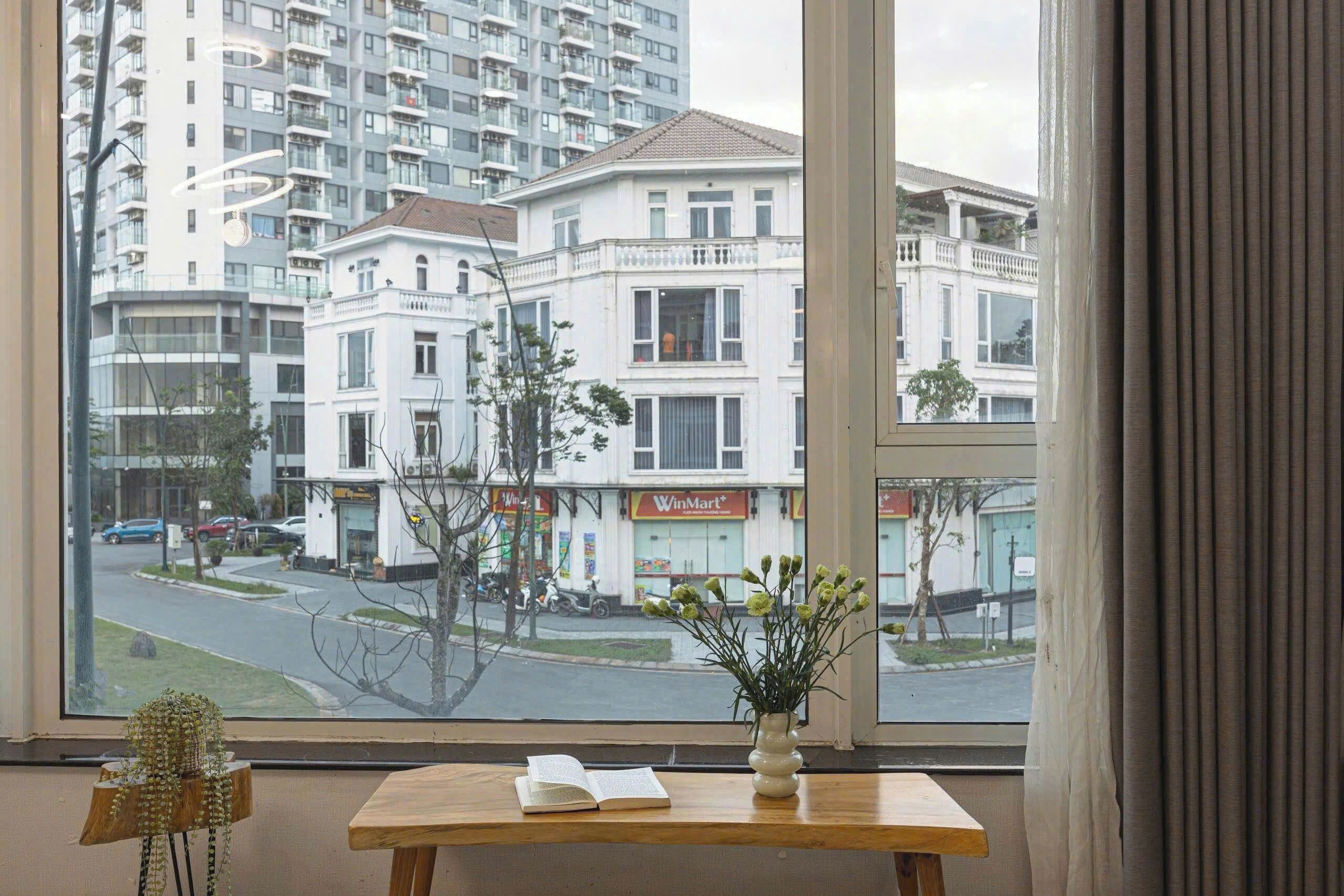 Vista desde una ventana con una mesa, un libro y un florero con flores.